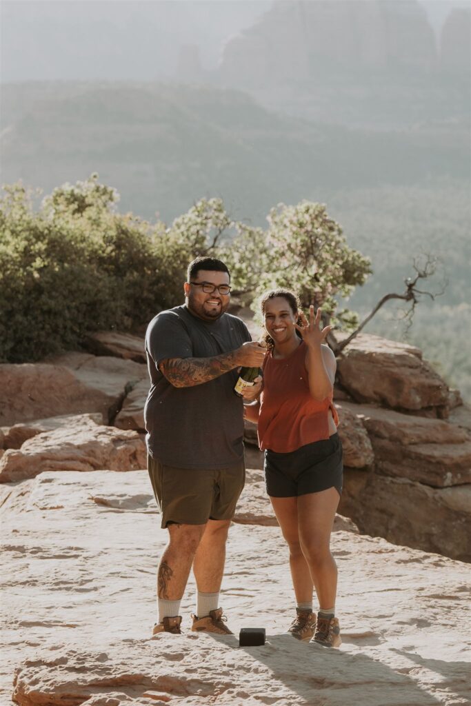 Celebrating the proposal! The newly engaged couple shares a joyful moment at Sedona's Devil's Bridge, with champagne and smiles, as she proudly shows off her ring.