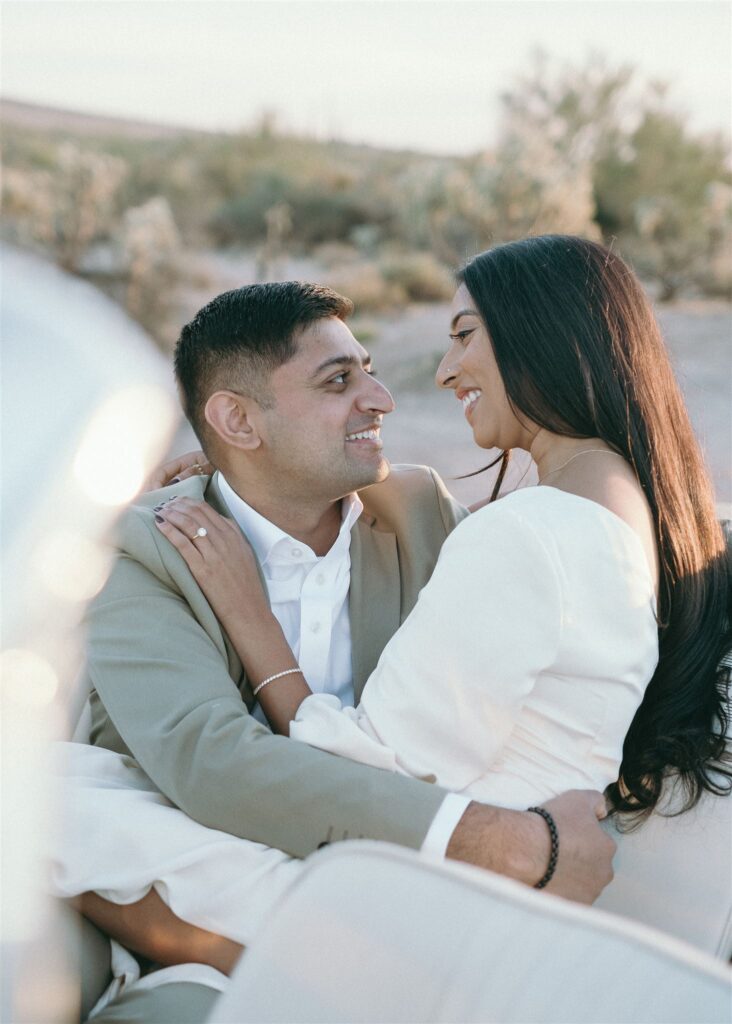 man and women smiling at each other in vintage car in the desert