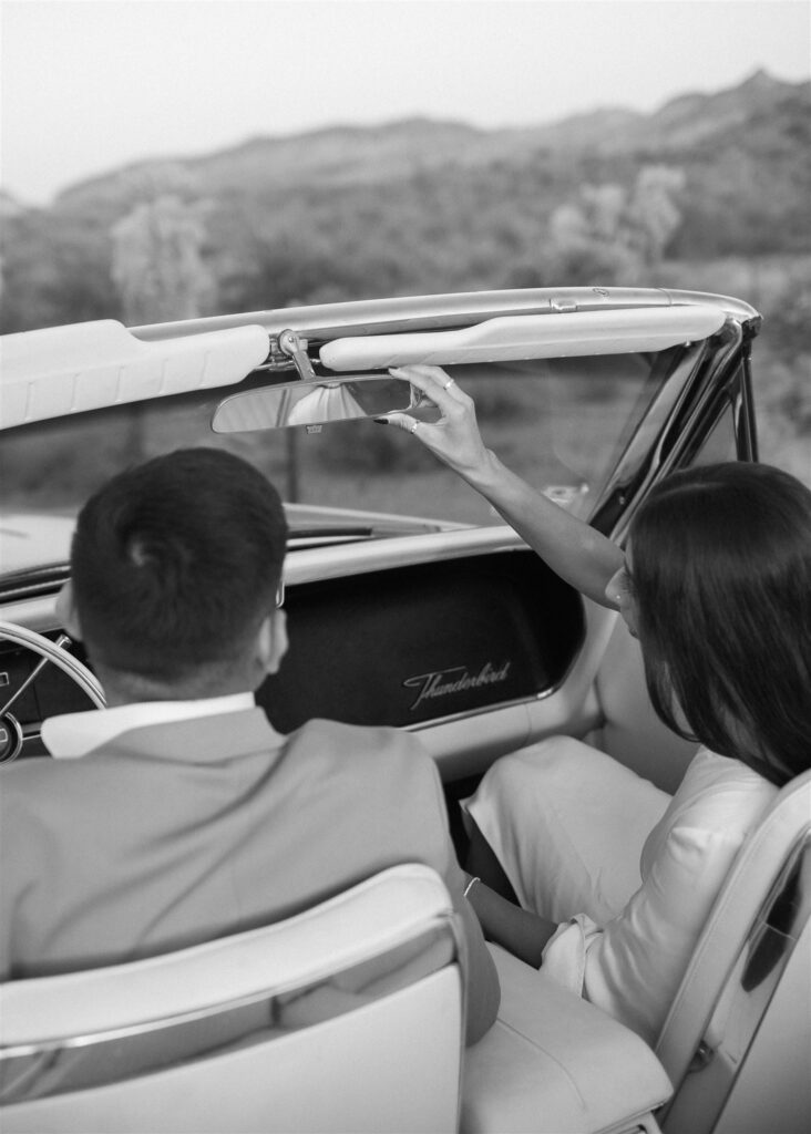 women adjusting mirror in vintage car sitting next to man