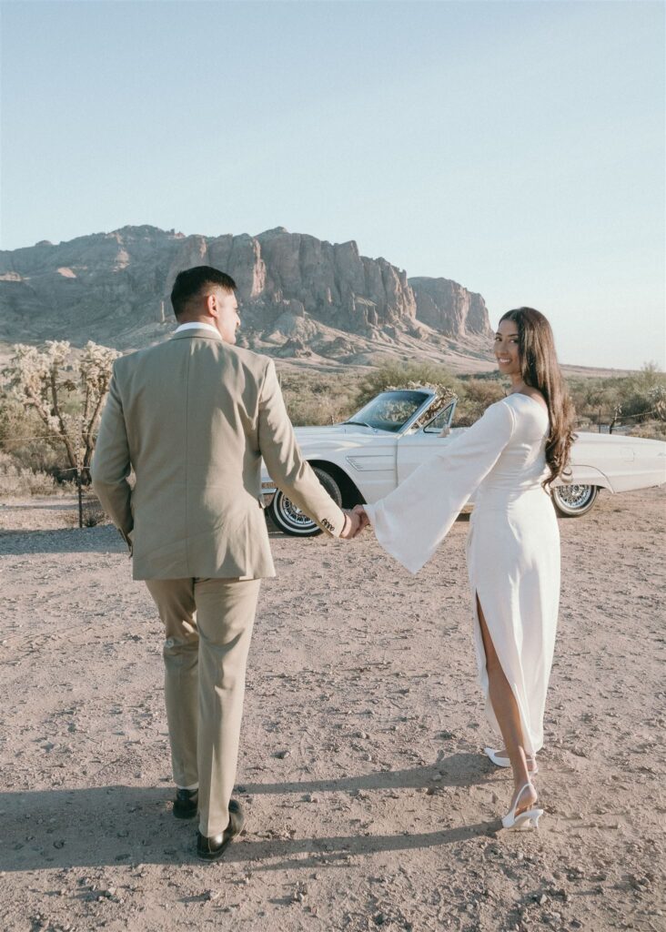 Man and women holding hands walking towards the desert with woman looking back and smiling