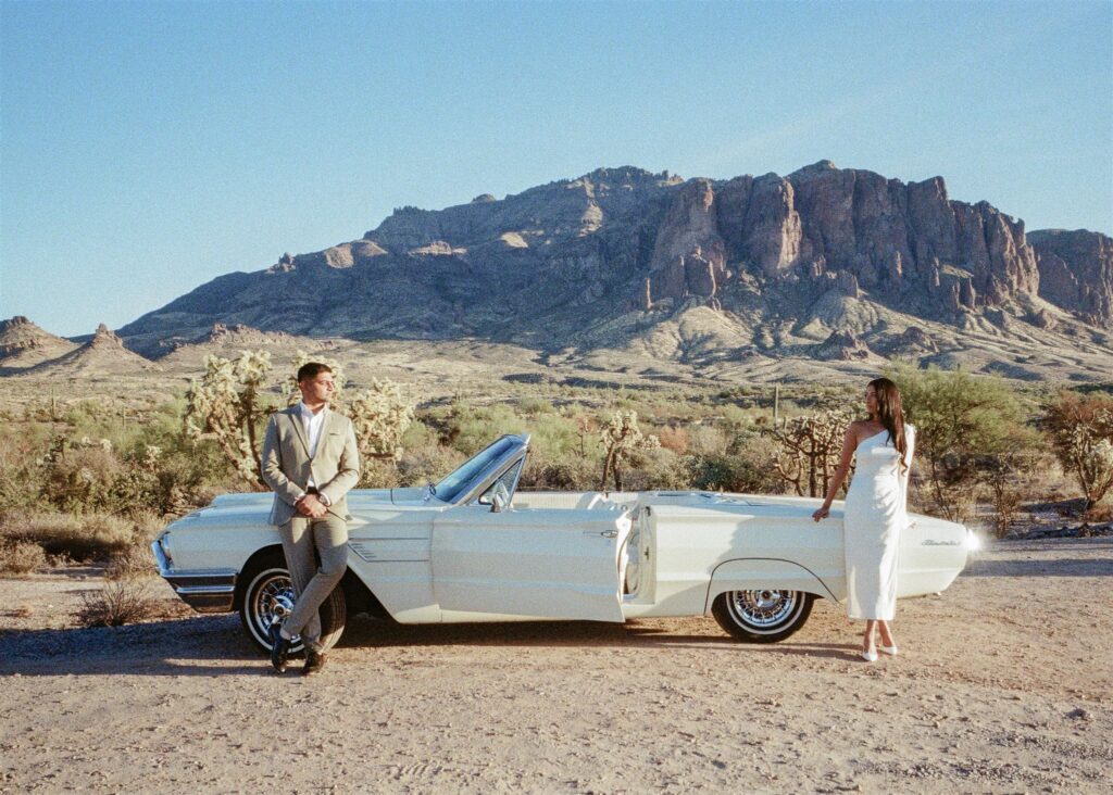 Man and women standing in front of a vintage car in the desert