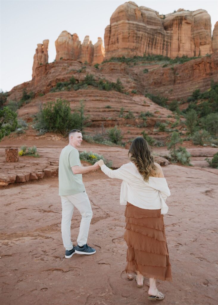 Cathedral Rock engagement photos in Sedona featuring a couple hiking and posing on red rock cliffs at sunset