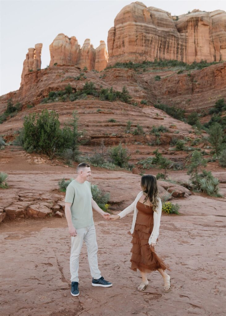 Cathedral Rock engagement photos in Sedona featuring a couple hiking and posing on red rock cliffs at sunset