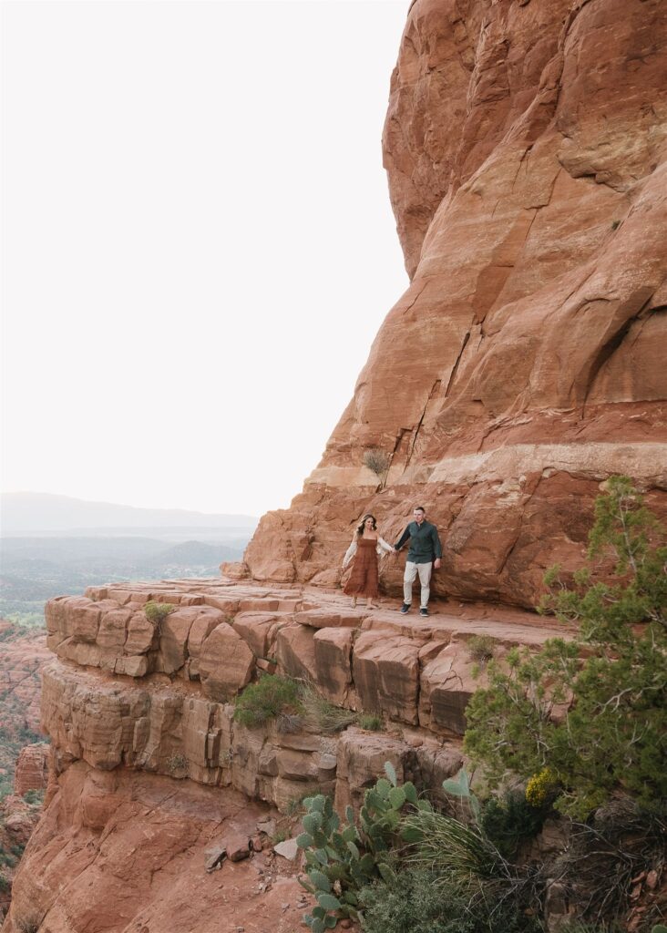 Cathedral Rock engagement photos in Sedona featuring a couple hiking and posing on red rock cliffs at sunset