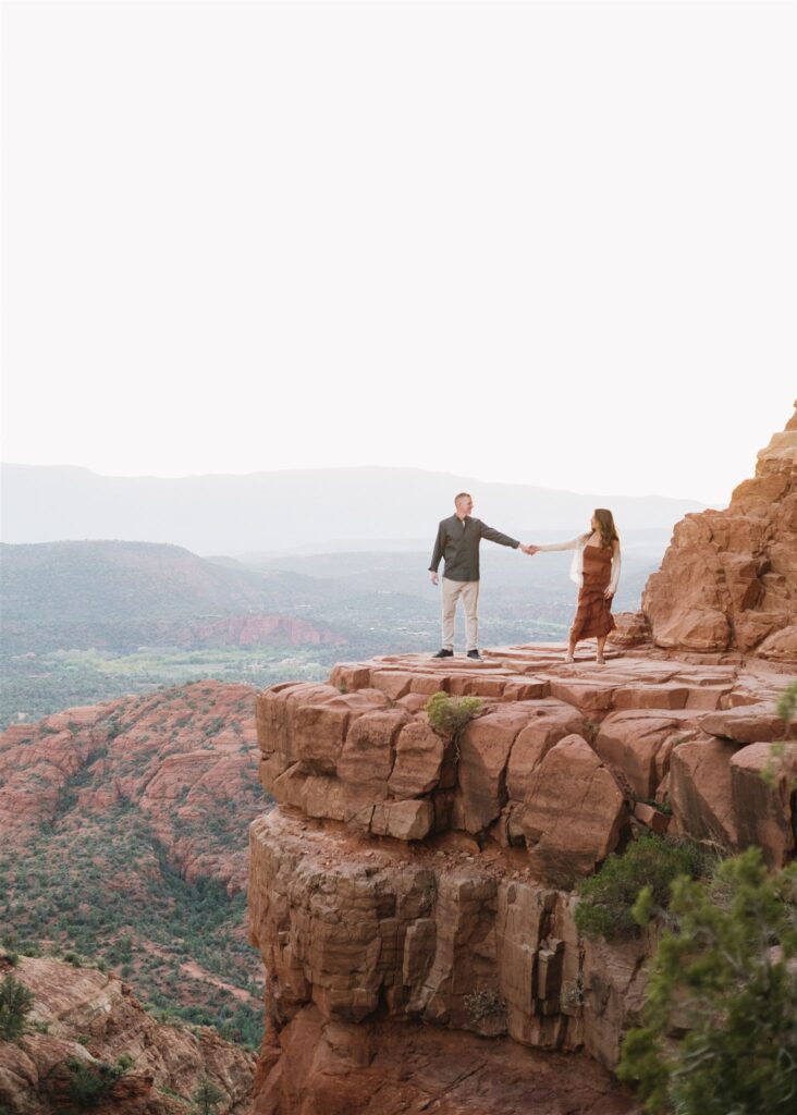 Cathedral Rock engagement photos in Sedona featuring a couple hiking and posing on red rock cliffs at sunset