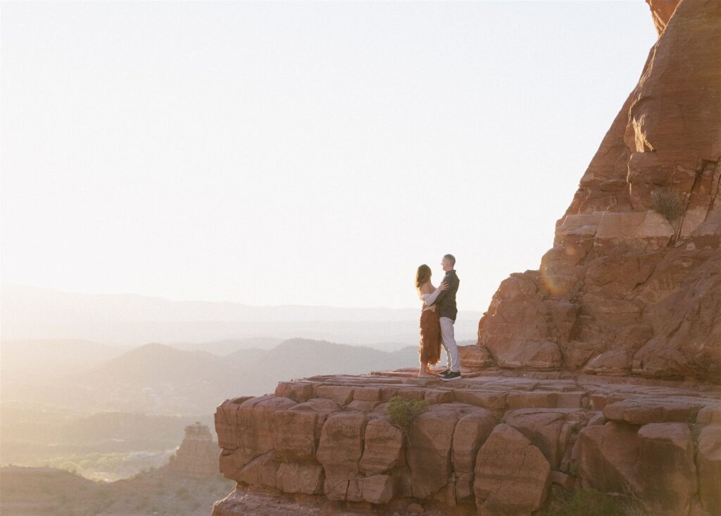 Cathedral Rock engagement photos in Sedona featuring a couple hiking and posing on red rock cliffs at sunset