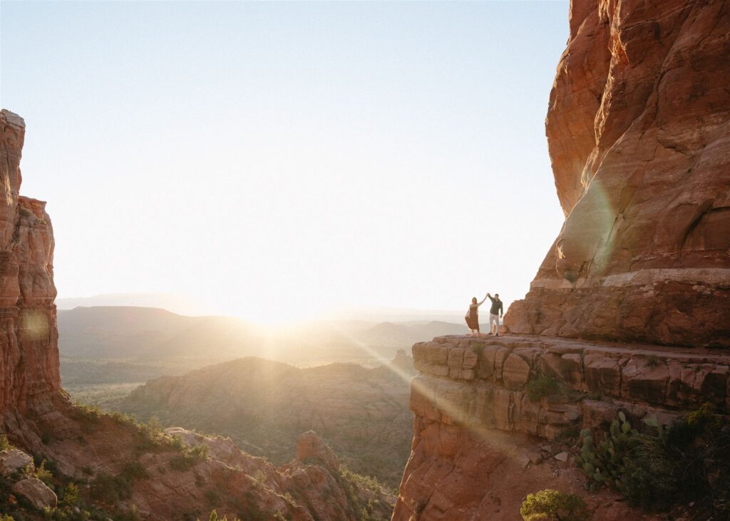 Cathedral Rock engagement photos in Sedona featuring a couple hiking and posing on red rock cliffs at sunset