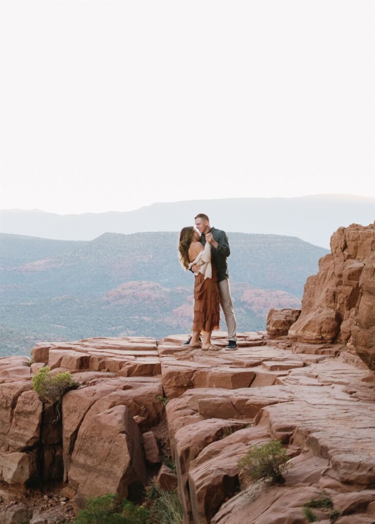 Cathedral Rock engagement photos in Sedona featuring a couple hiking and posing on red rock cliffs at sunset