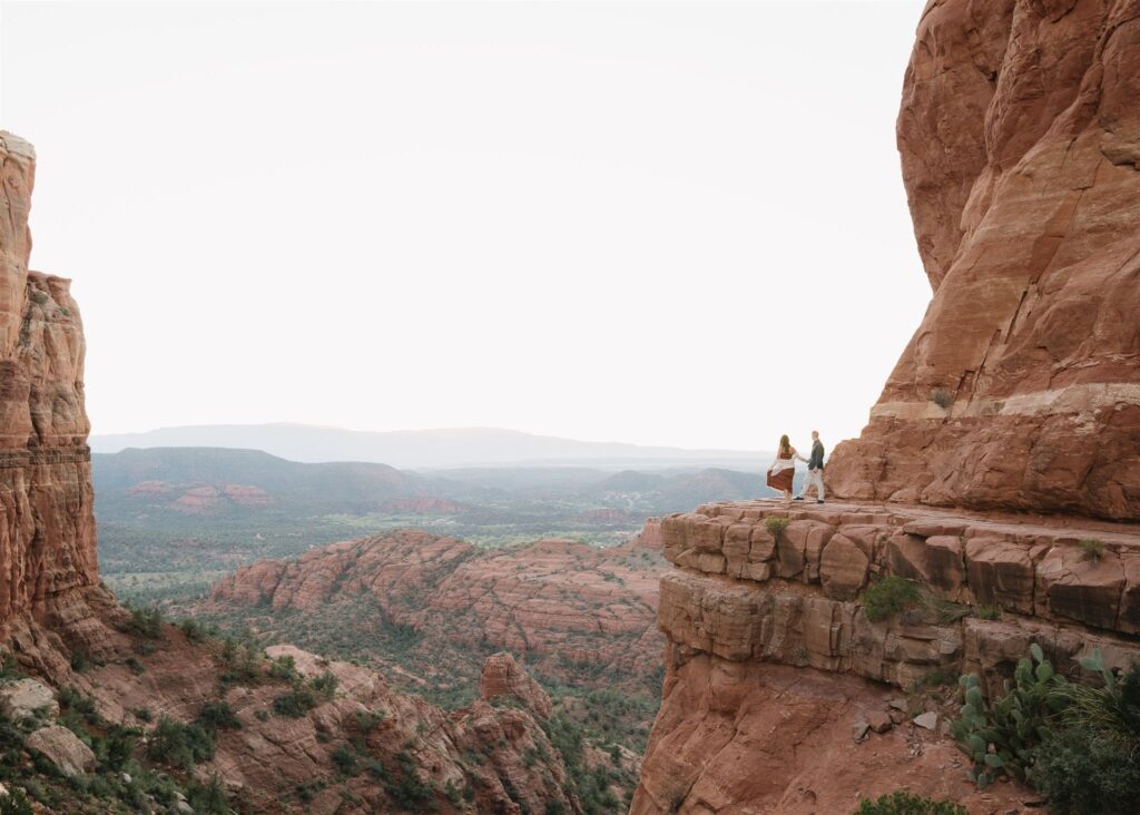 Cathedral Rock engagement photos in Sedona featuring a couple hiking and posing on red rock cliffs at sunset
